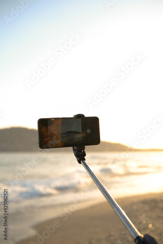 Someone makes photos on mobile phone with selfie stick on sunset sea beach.