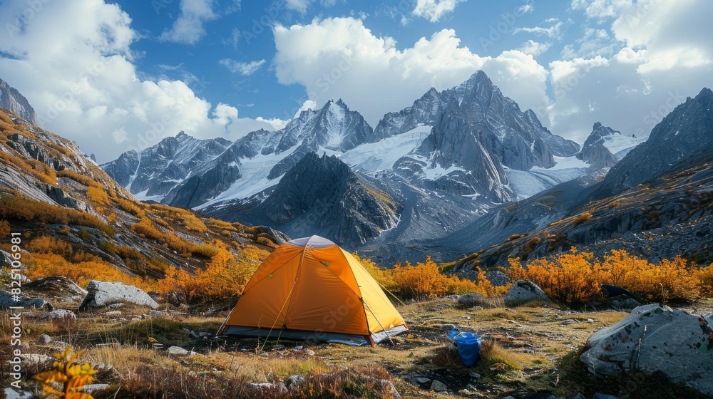 A small orange tent is set up in a field next to a mountain