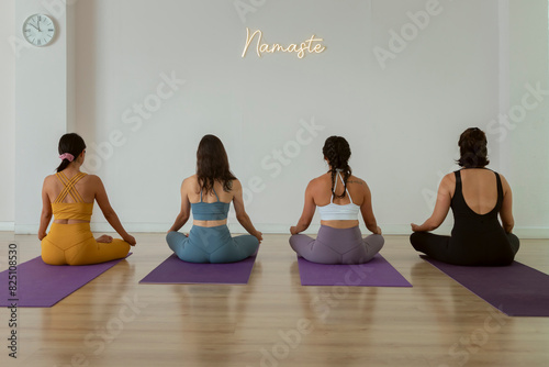 4 women meditating sitting in lotus in a yoga studio with a namaste sign on the wall