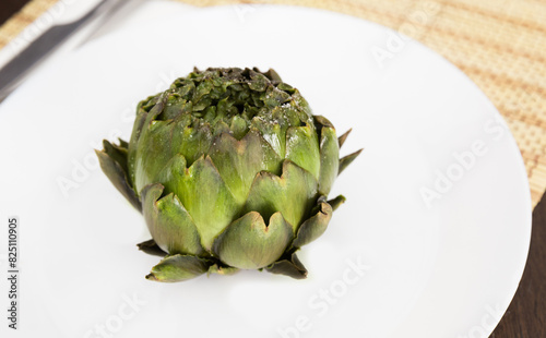 Cooked whole artichoke on a white plate