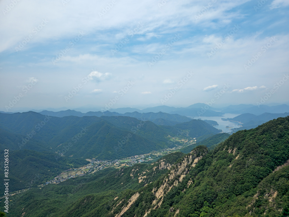 Naklejka premium A mountain range with a city in the valley below. The sky is clear and blue. The mountains are covered in trees and the city is small and quaint