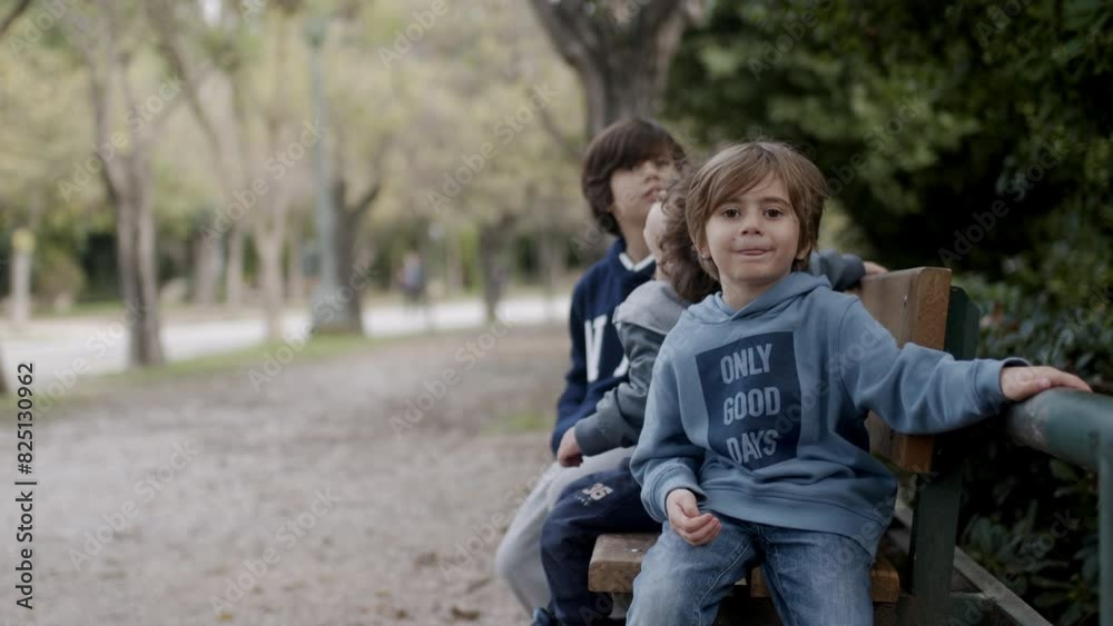 Three boys relax and play on a park bench on a cool autumn day, surrounded by trees and greenery. Three boys relax and play on a park bench on a cool autumn day, surrounded by trees and greenery.