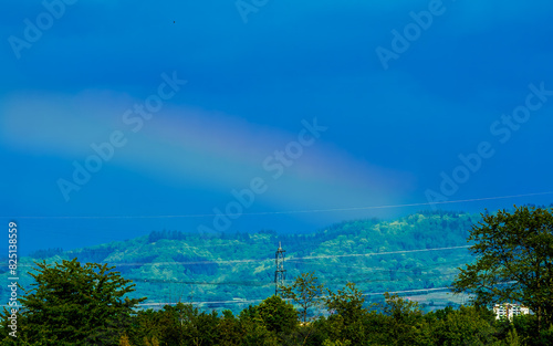 Rainbow in dark blue sky over wooded hills