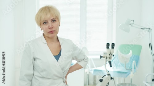 Portrait of a female doctor in the gynecologist's office. An examination chair and a colposcope can be seen behind her. High quality 4k footage photo