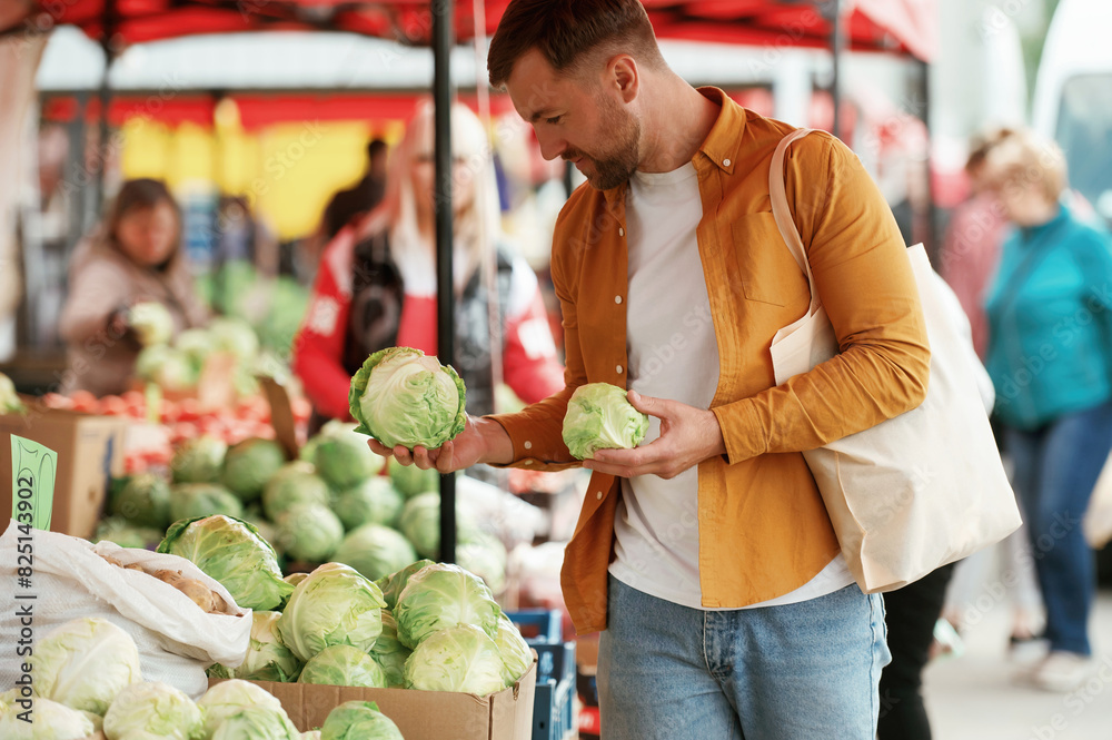 Fototapeta premium Choosing cabbage. Handsome man is on the street market or bazaar