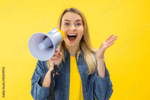 Smiling Young woman screaming in megaphone posing isolated on yellow background studio