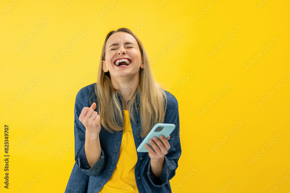 Yes, Great News. Portrait Of Excited Woman Celebrating Win, Using Smartphone, Smiling Young Lady Having Success, Holding Cellphone, Yellow Studio Background