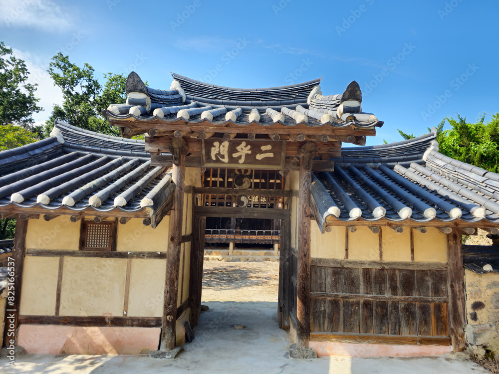 Naklejka premium A building with a large wooden door and a roof with Chinese characters on it. The building appears to be a temple or a shrine