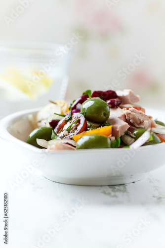 Salad with tuna, green olives and cherry tomatoes. Bright wooden background. Close up. Copy space.