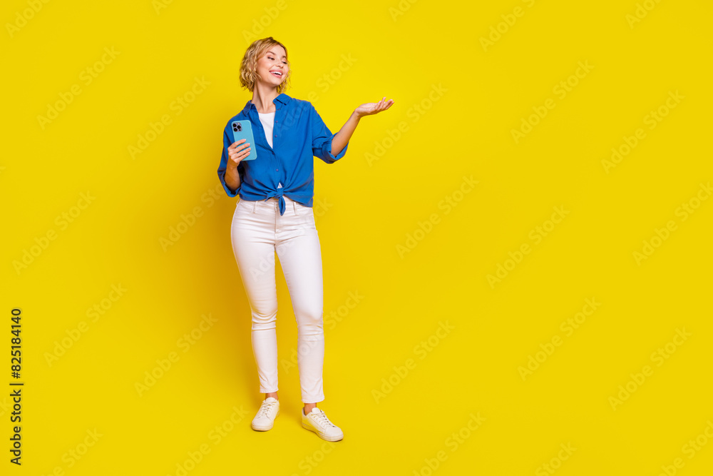 Full size portrait of pretty young lady arm hold phone empty space wear shirt isolated on yellow color background Full size portrait of pretty young lady arm hold phone empty space wear shirt isolated on yellow color background