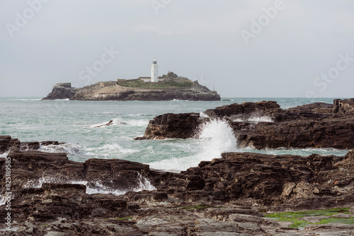 Waves crashing against rocks with Godrevy Lighthouse beyond. photo