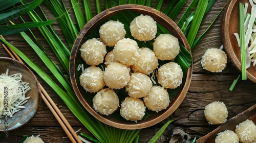 Traditional khanom tom (coconut balls) arranged neatly on a wooden plate surrounded by pandan leaves photo