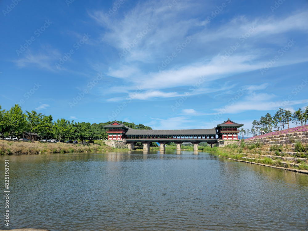 A bridge spans a river with a clear blue sky above. The bridge is surrounded by trees and a lush green area A bridge spans a river with a clear blue sky above. The bridge is surrounded by trees and a lush green area