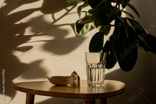 Table with glass of water with shadow of houseplant on the wall photo