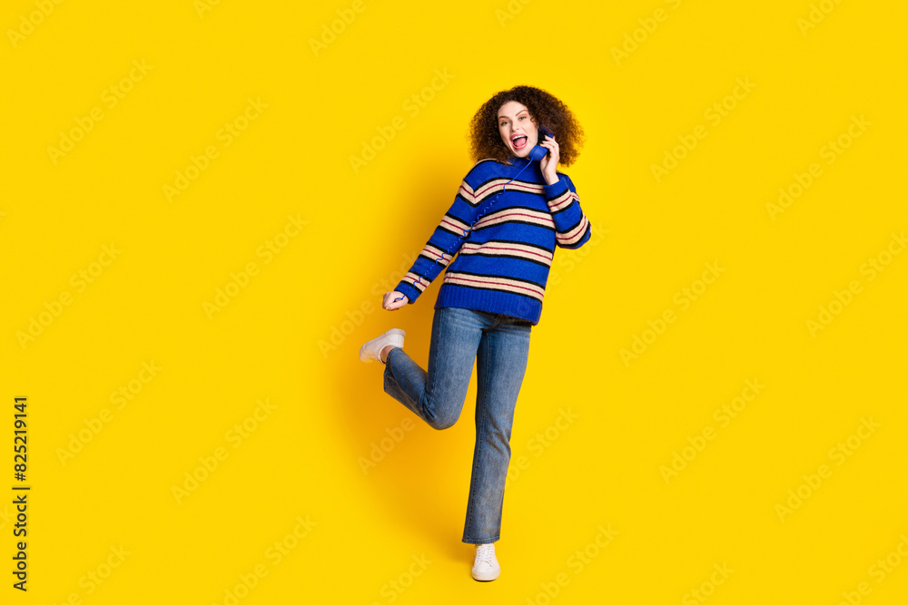 Portrait of ecstatic woman with wavy hair wear knit sweater talk on landline phone stand on one leg isolated on yellow color background Portrait of ecstatic woman with wavy hair wear knit sweater talk on landline phone stand on one leg isolated on yellow color background