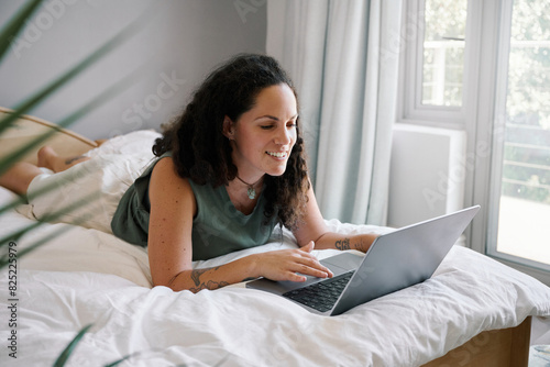 Smiling woman surfing internet via laptop on bed photo