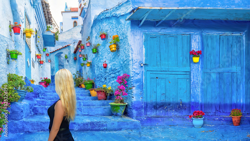 A blonde haired woman in a colourful backstreet with potted plants in Chefchaouen, Morocco. photo