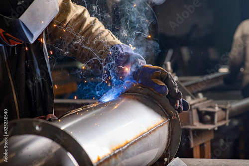 Male welder wearing a protective mask is welding stainless pipe