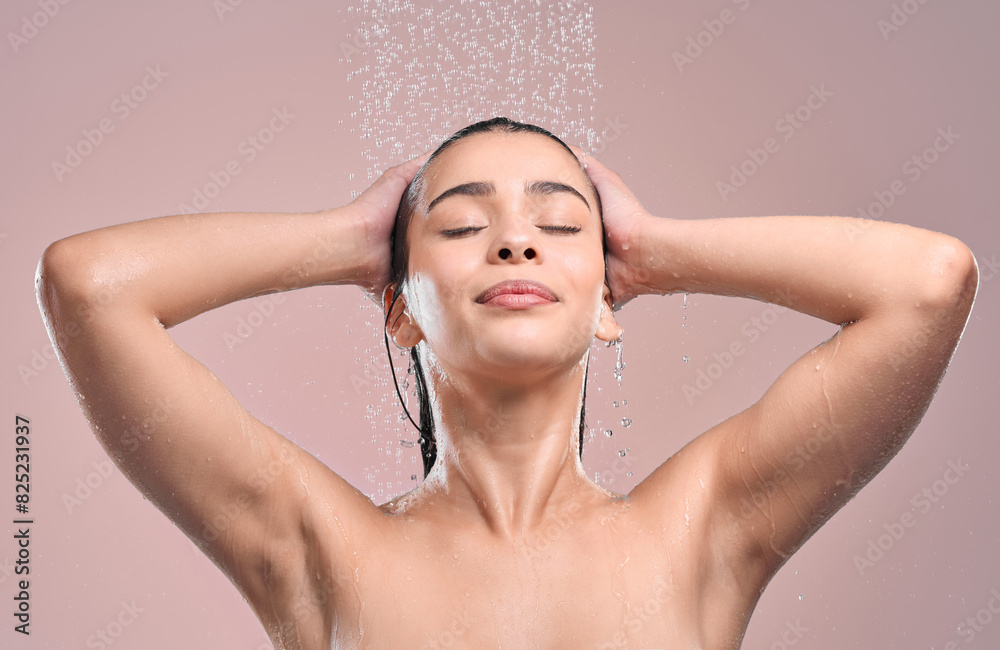 Naklejka premium Woman, hair and shower in studio with water, pink background and relaxing for cleaning or model washing. Grooming, hygiene and female person wet for self care, eyes closed and wellness routine