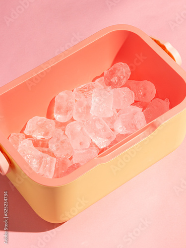 Pink and yellow container filled with ice cubes against a soft pink background. Showcases a minimalistic and modern, perfect for themes related to summer, freshness, and cool beverages.