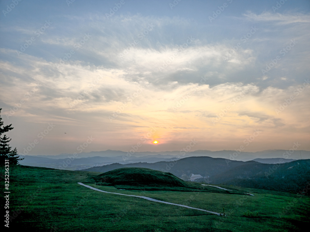 A beautiful sunset over a mountain range with a clear blue sky. The sun is setting and the sky is filled with clouds A beautiful sunset over a mountain range with a clear blue sky. The sun is setting and the sky is filled with clouds