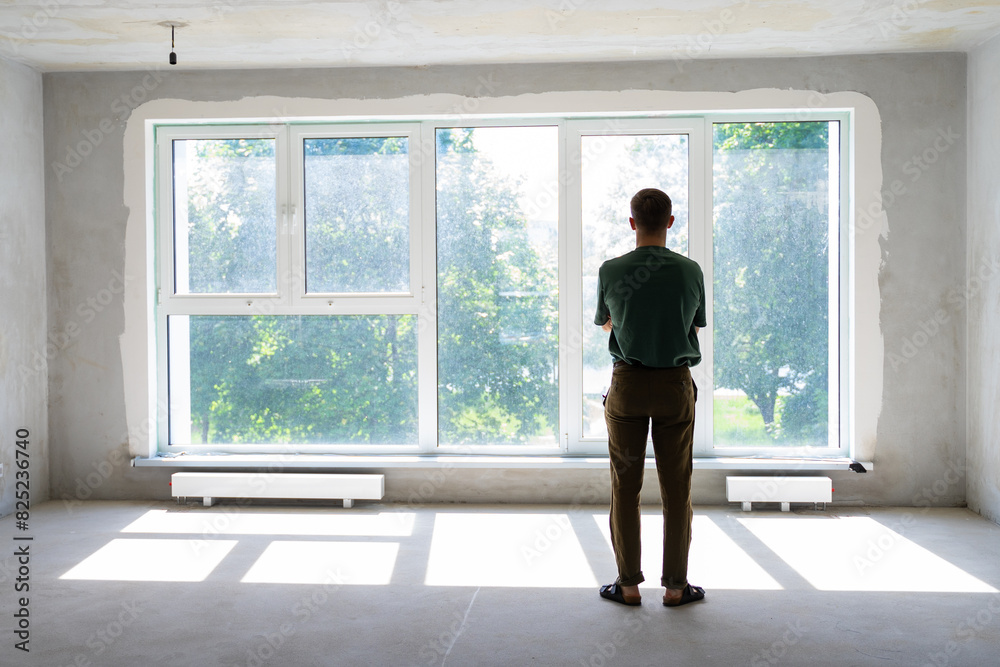 unrecognizable millennial man in front of window in a new empty home unrecognizable millennial man in front of window in a new empty home