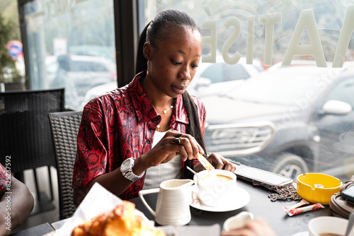 Woman Enjoying Coffee and Croissant at a Sunlit Café Table During Brea photo