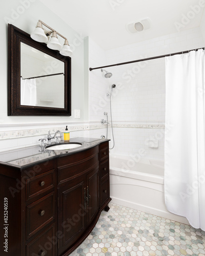 A bathroom with a dark mahogany vanity cabinet  hexagon tile flooring  and a shower with white subway tiles.