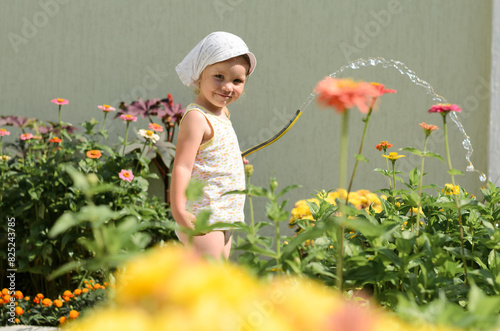 little girl watering flowers with water in the yard photo