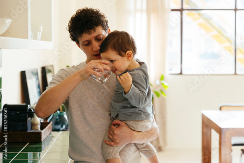 Father with toddler son drinking a glass of water at modern home