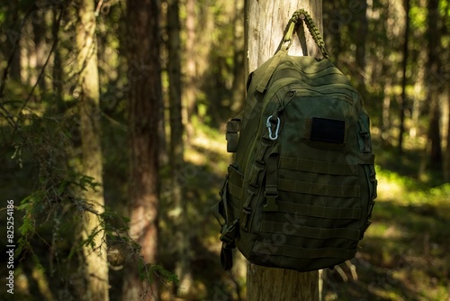 Tactical backpack on tree trunk in forest .
