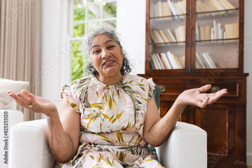 At home on video call, a senior biracial woman wearing a floral dress, gesturing