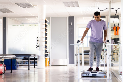 A biracial male patient walking at gym rehabilitation center between parallel bars, copy space photo