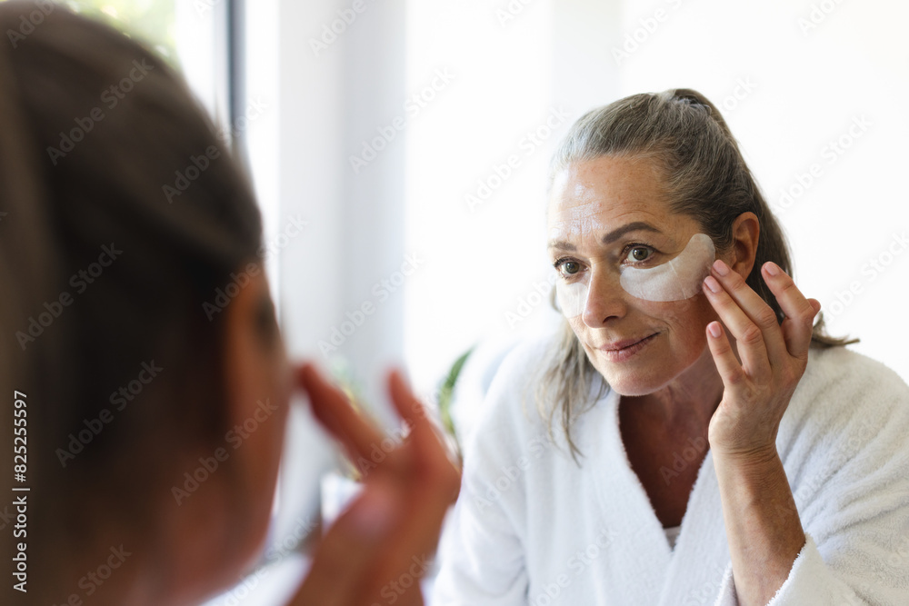 At bathroom at home, mature Caucasian woman applying facial mask, looking in mirror At bathroom at home, mature Caucasian woman applying facial mask, looking in mirror