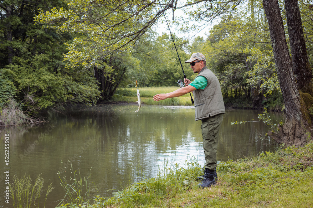 An angler standing on a riverbank and successfully catching a fish during freshwater fishing season. Concepts of individual sport and leisure activity. An angler standing on a riverbank and successfully catching a fish during freshwater fishing season. Concepts of individual sport and leisure activity.