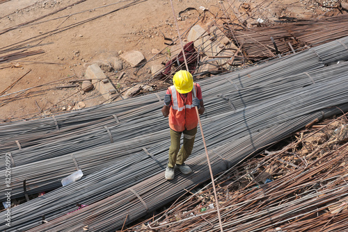 A builder in a yellow helmet works with iron reinforcement. Top view of the construction site. Candid photo.