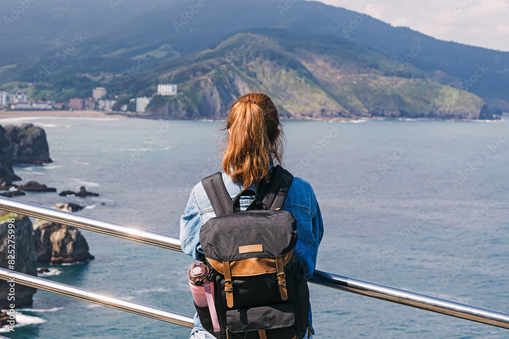 Fototapeta premium Woman tourist with a backpack looking on the scenic landscape at San Sebastian, Spain