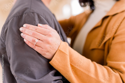 An engaged couple embracing. She has her ring hand on his arm. They wear fall, casual clothes.