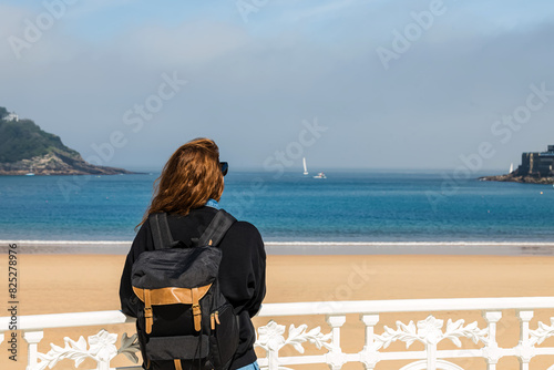 View from the back of the woman tourist with a backpack looking on the beach of San Sebastian, Spain