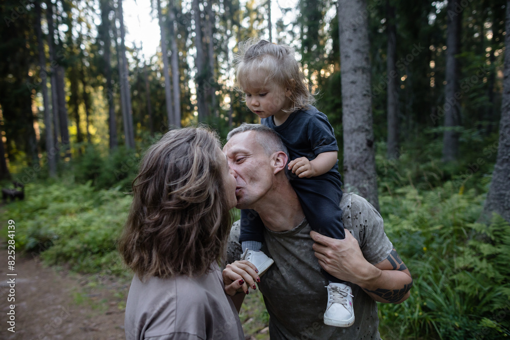 Spouses kiss with little child on the shoulders Spouses kiss with little child on the shoulders