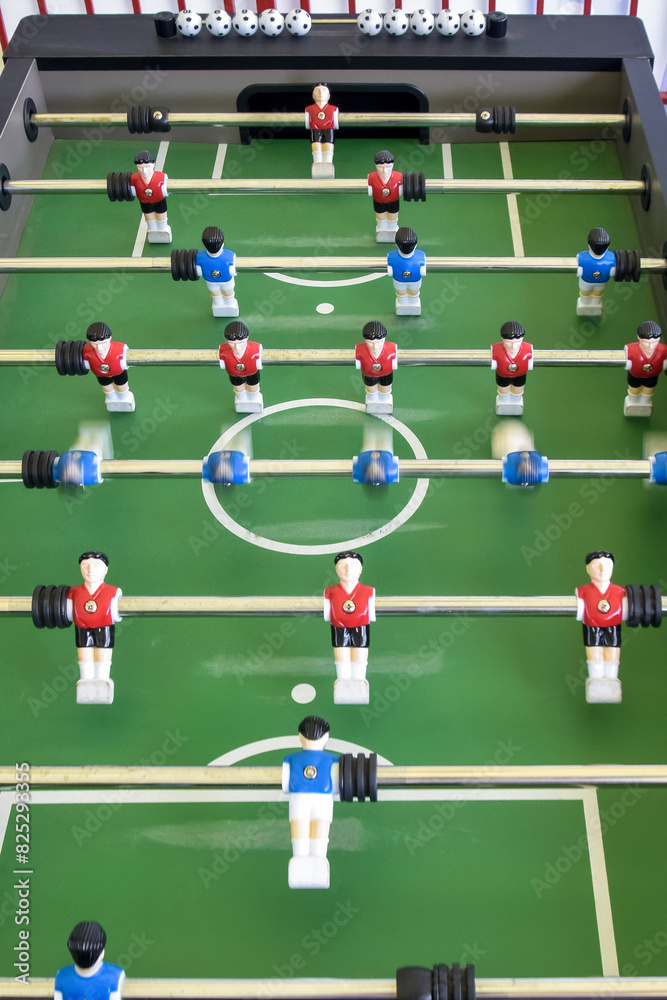 Classic Foosball Table Game With Players in Red and Blue Jerseys During Daytime Indoor Match. Close-up view of foosball table featuring red and blue jersey players positioned for daytime indoor game. Classic Foosball Table Game With Players in Red and Blue Jerseys During Daytime Indoor Match. Close-up view of foosball table featuring red and blue jersey players positioned for daytime indoor game.