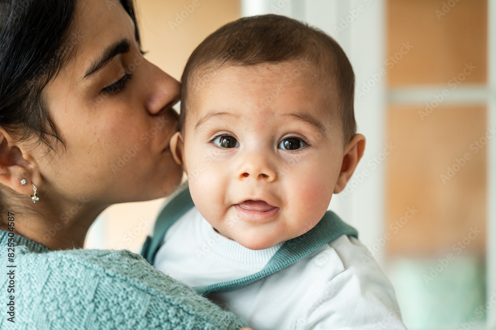 Young woman lovingly kisses her adorable baby on the cheek Young woman lovingly kisses her adorable baby on the cheek