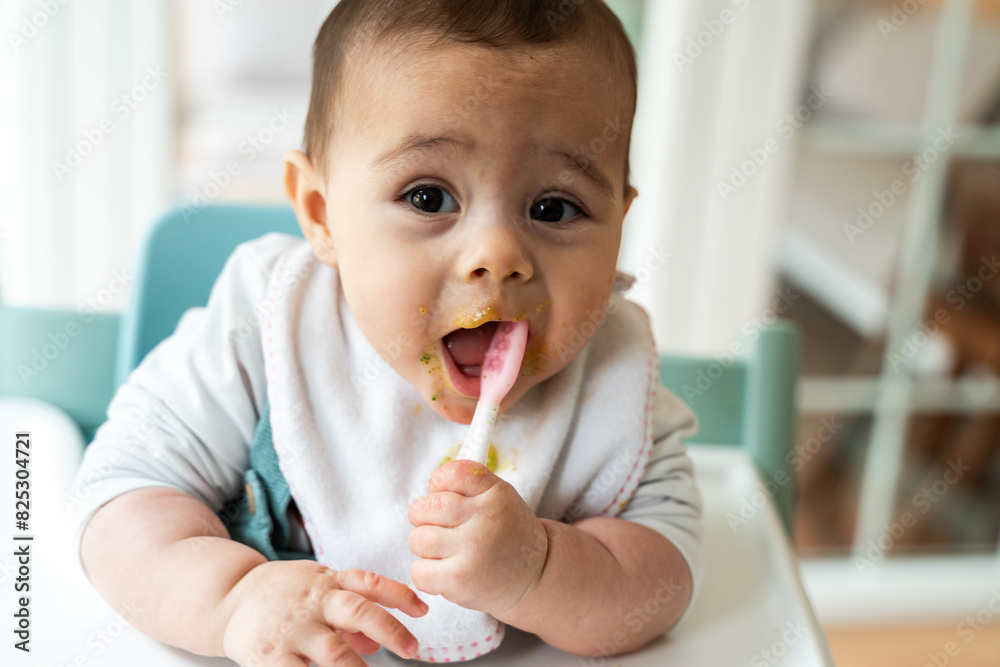 Messy baby enjoying first solids in high chair Messy baby enjoying first solids in high chair