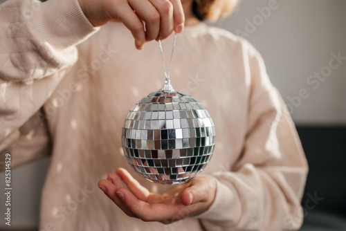 Close-up of the hands of a girl holding a disco ball against the background of a decorated Christmas tree. Celebration atmosphere
