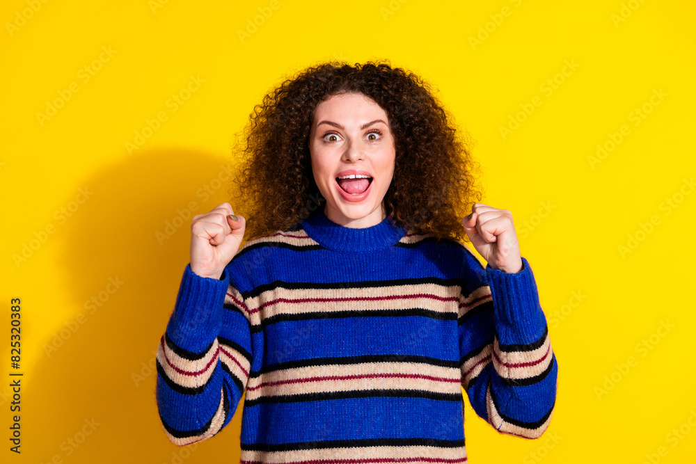 Portrait of ecstatic girl with wavy hair wear knit pullover clenching fists win lottery scream yeah isolated on yellow color background Portrait of ecstatic girl with wavy hair wear knit pullover clenching fists win lottery scream yeah isolated on yellow color background