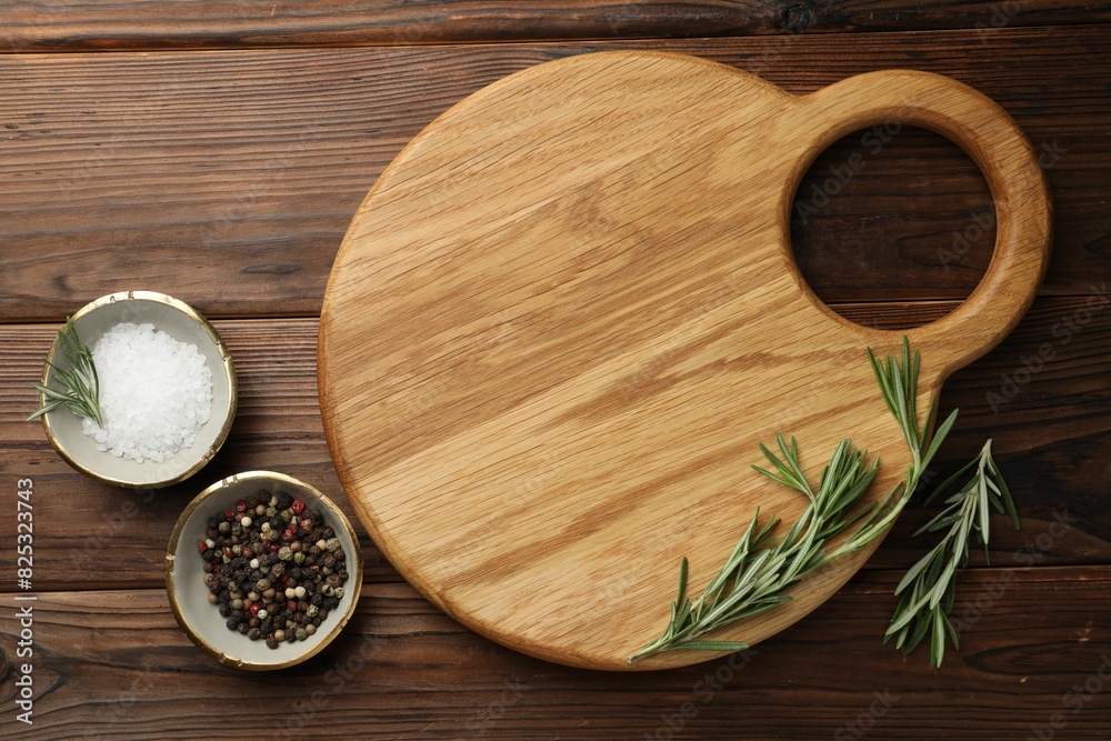 Cutting board, salt, pepper and rosemary on wooden table, flat lay. Space for text Cutting board, salt, pepper and rosemary on wooden table, flat lay. Space for text