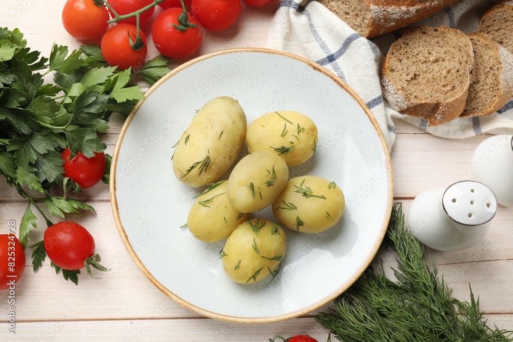 Plate with young boiled potatoes and products on light wooden table, flat lay