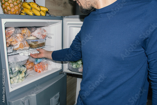 Man Taking Ice Cubes from Fridge with Frozen Ingredients photo