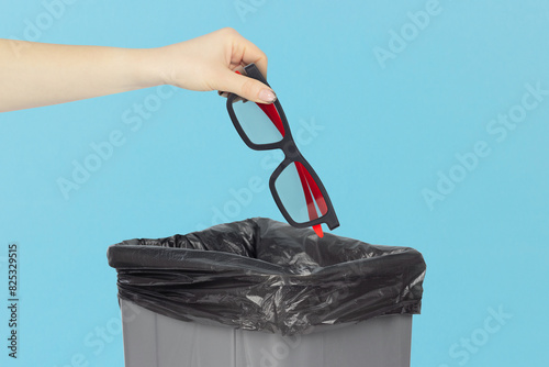 throw the plastic glasses for watching 3D cinema in the cinema into the trash, outstretched hand with sunglasses in front of the trash can, plastic recycling concept
