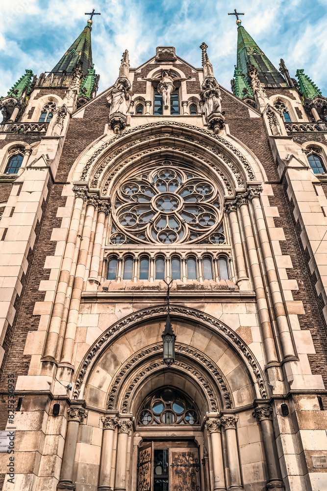 Fototapeta premium Bottom view of the Church of Sts. Olha and Elizabeth portal in Lviv, Ukraine. Beautiful facade of a neo-Gothic temple with religious sculptures and a round rose window, architect Teodor Talowski, 1911